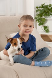 Photo of Little boy with his cute dog on sofa at home. Adorable pet
