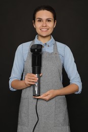 Beautiful young woman holding sous vide cooker on black background