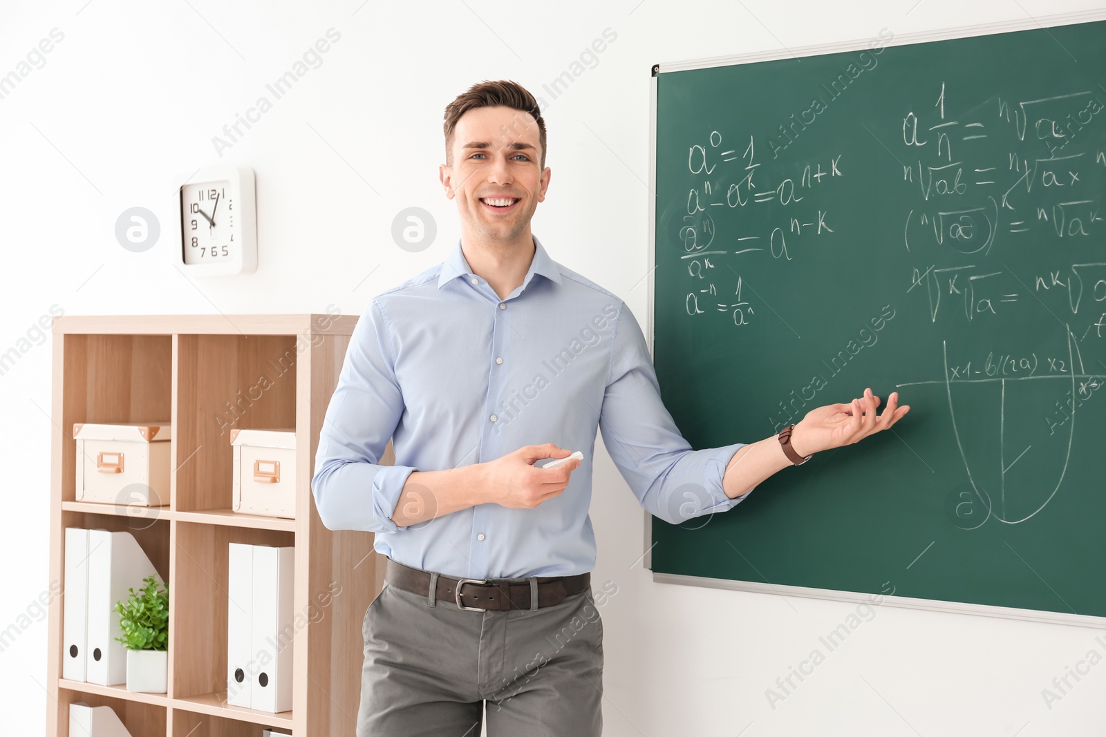 Photo of Young male teacher explaining math formulas written on blackboard in classroom