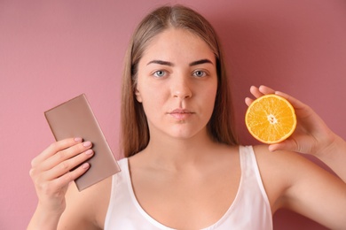 Photo of Young woman with acne problem holding orange and chocolate bar on color background. Skin allergy