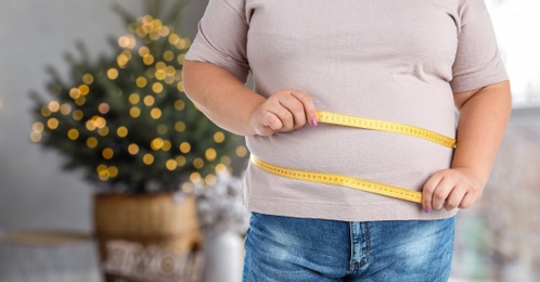 Image of Overweight woman measuring her waist in room decorated for Christmas after holidays, closeup
