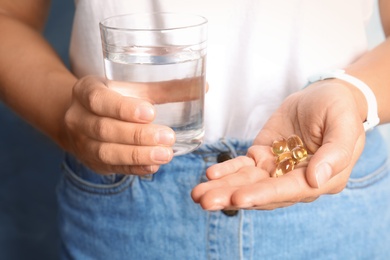 Woman with fish oil pills and glass of water, closeup