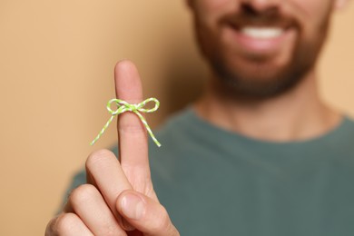 Man showing index finger with tied bow as reminder against beige background, focus on hand