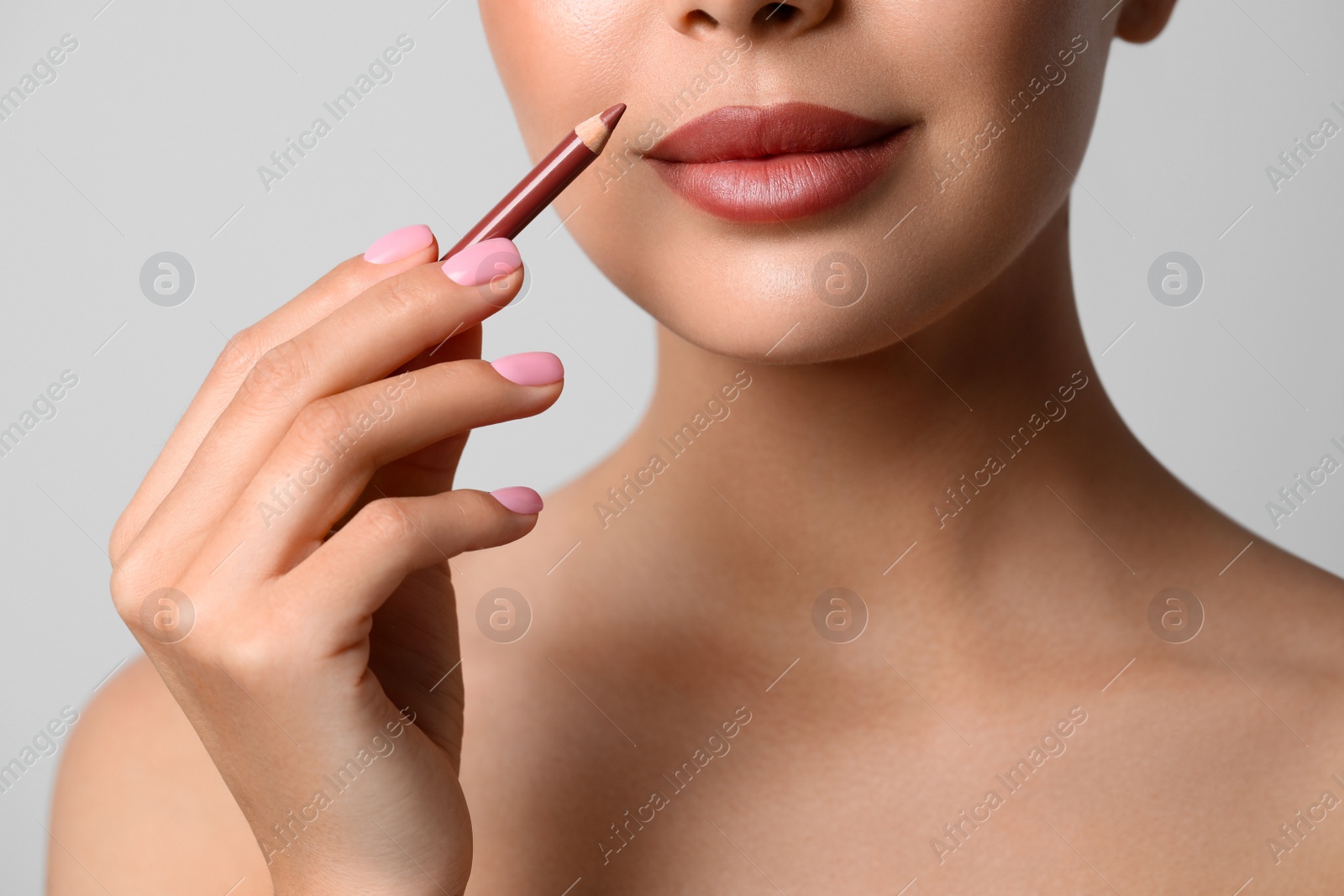 Photo of Young woman applying beautiful nude lip pencil on light grey background, closeup