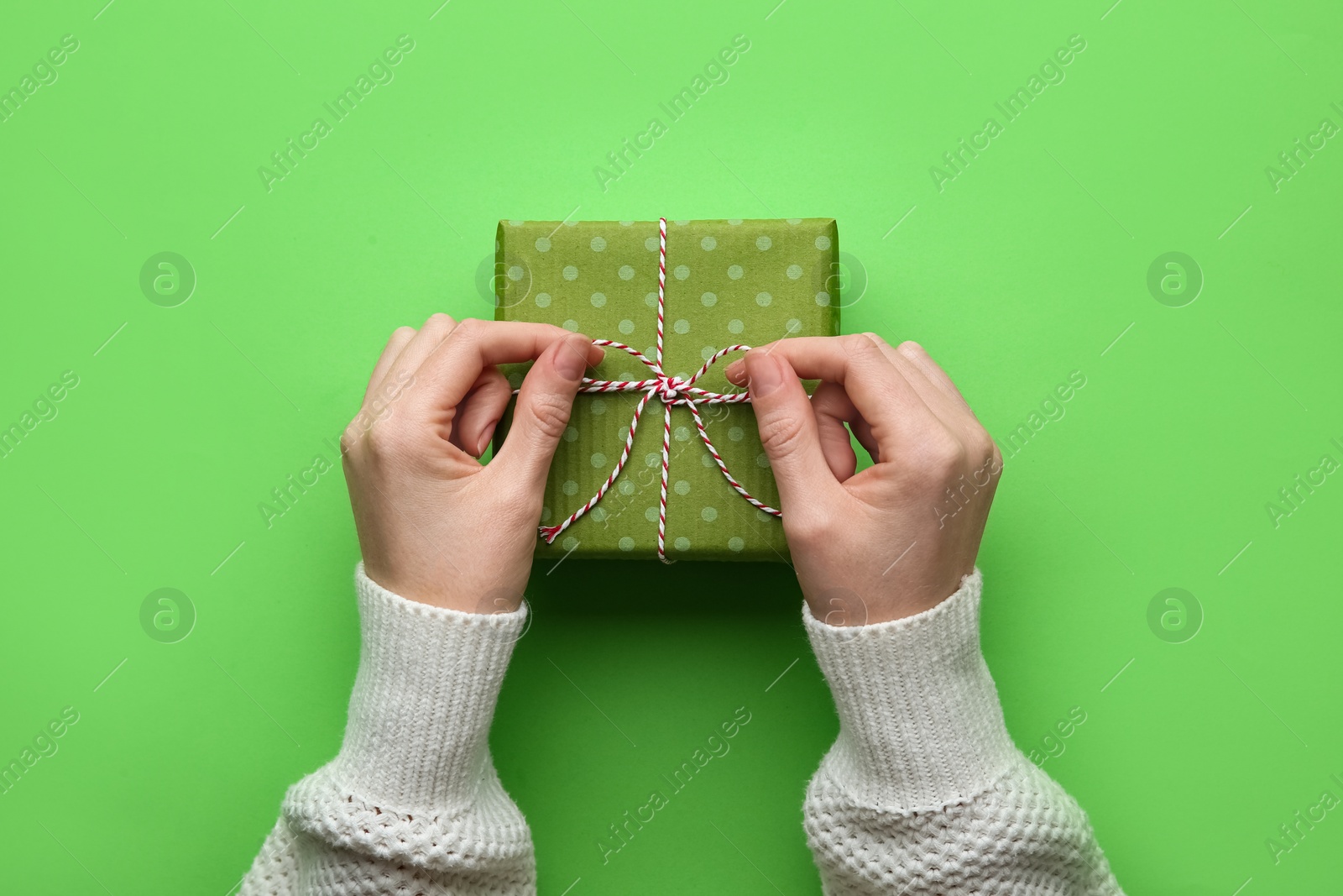 Photo of Woman holding Christmas gift box on green background, top view