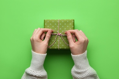 Photo of Woman holding Christmas gift box on green background, top view