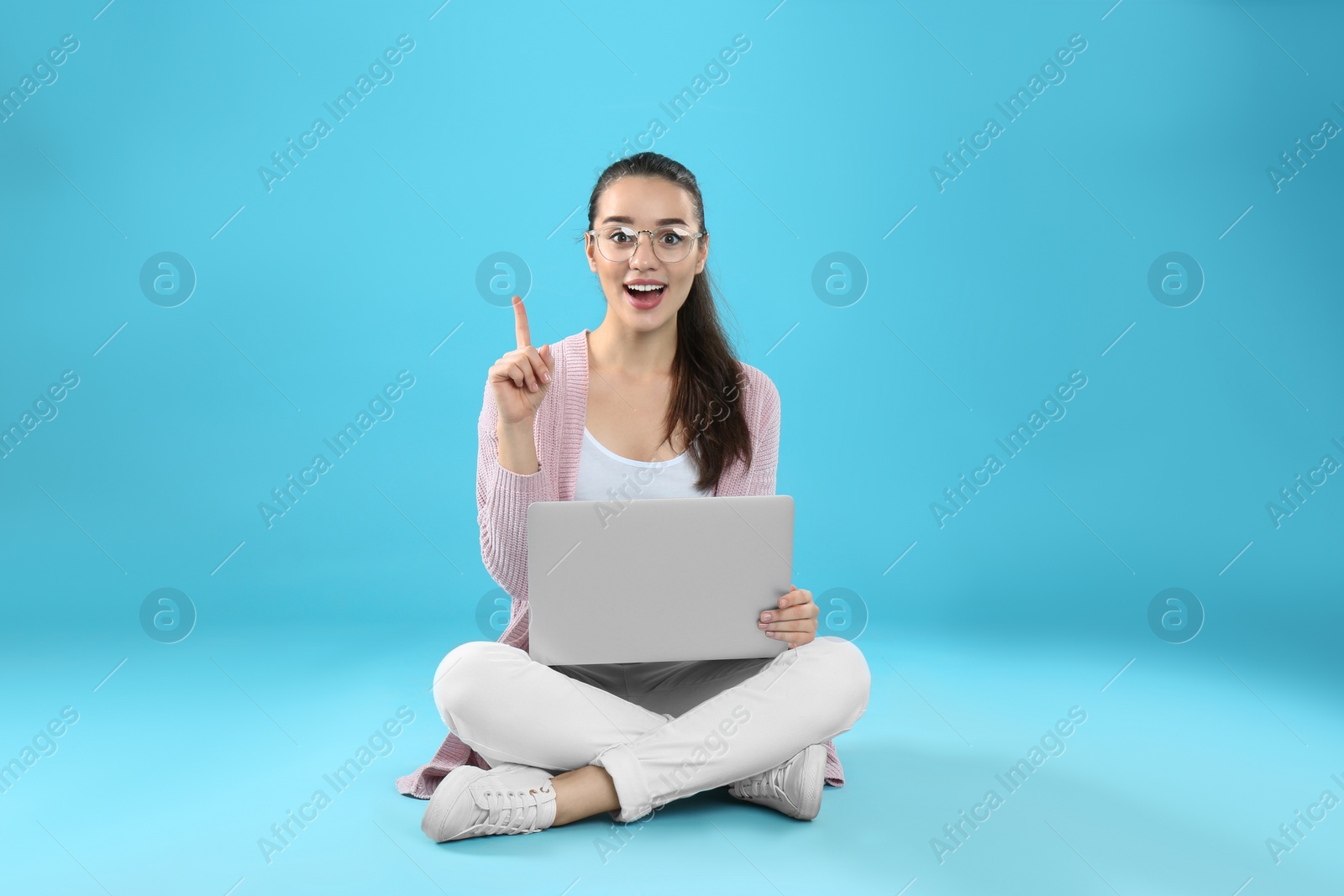 Photo of Young woman in casual outfit with laptop sitting on color background