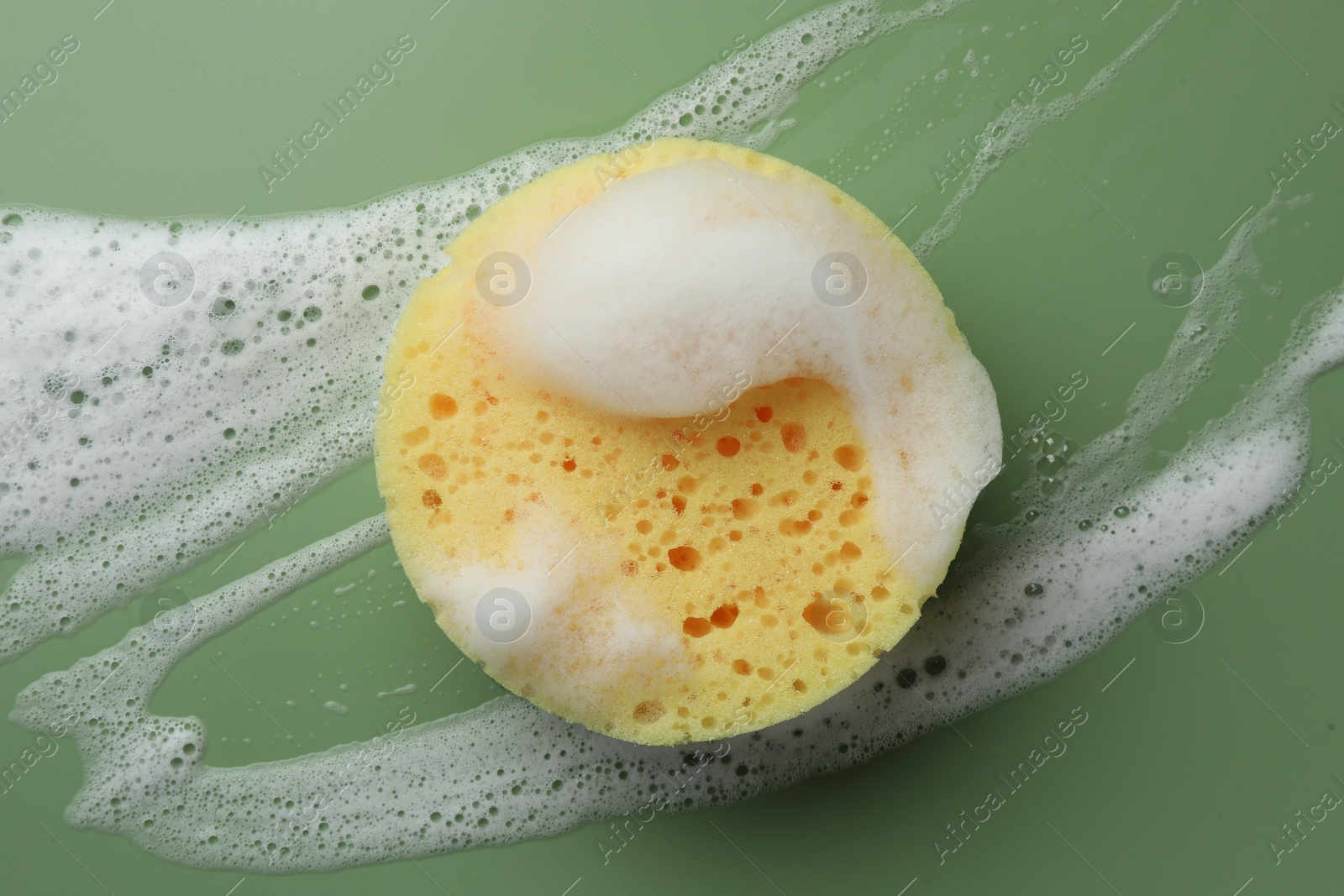 Photo of Yellow sponge with foam on green background, top view