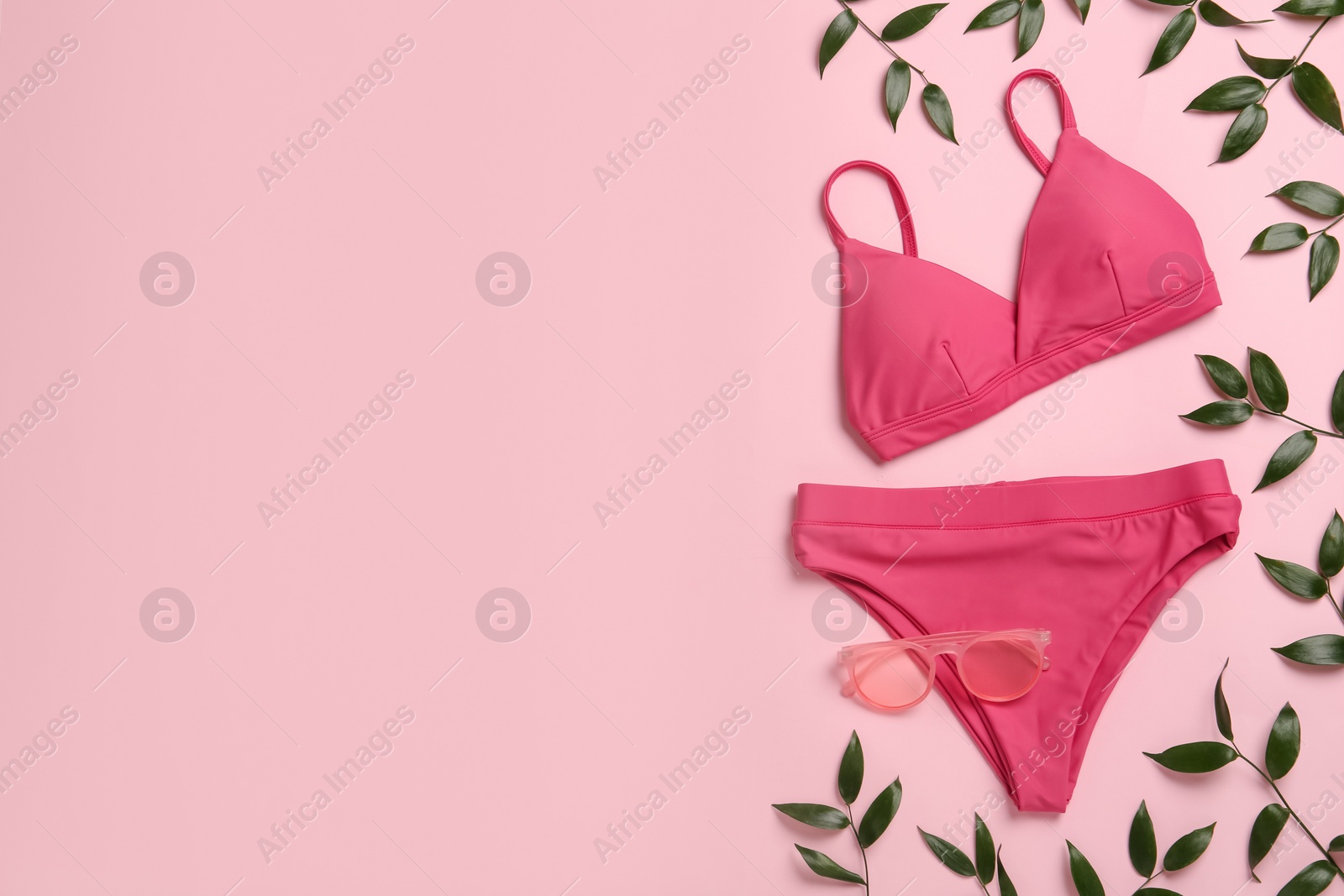 Photo of Stylish bikini, sunglasses and green leaves on pink background, flat lay. Space for text