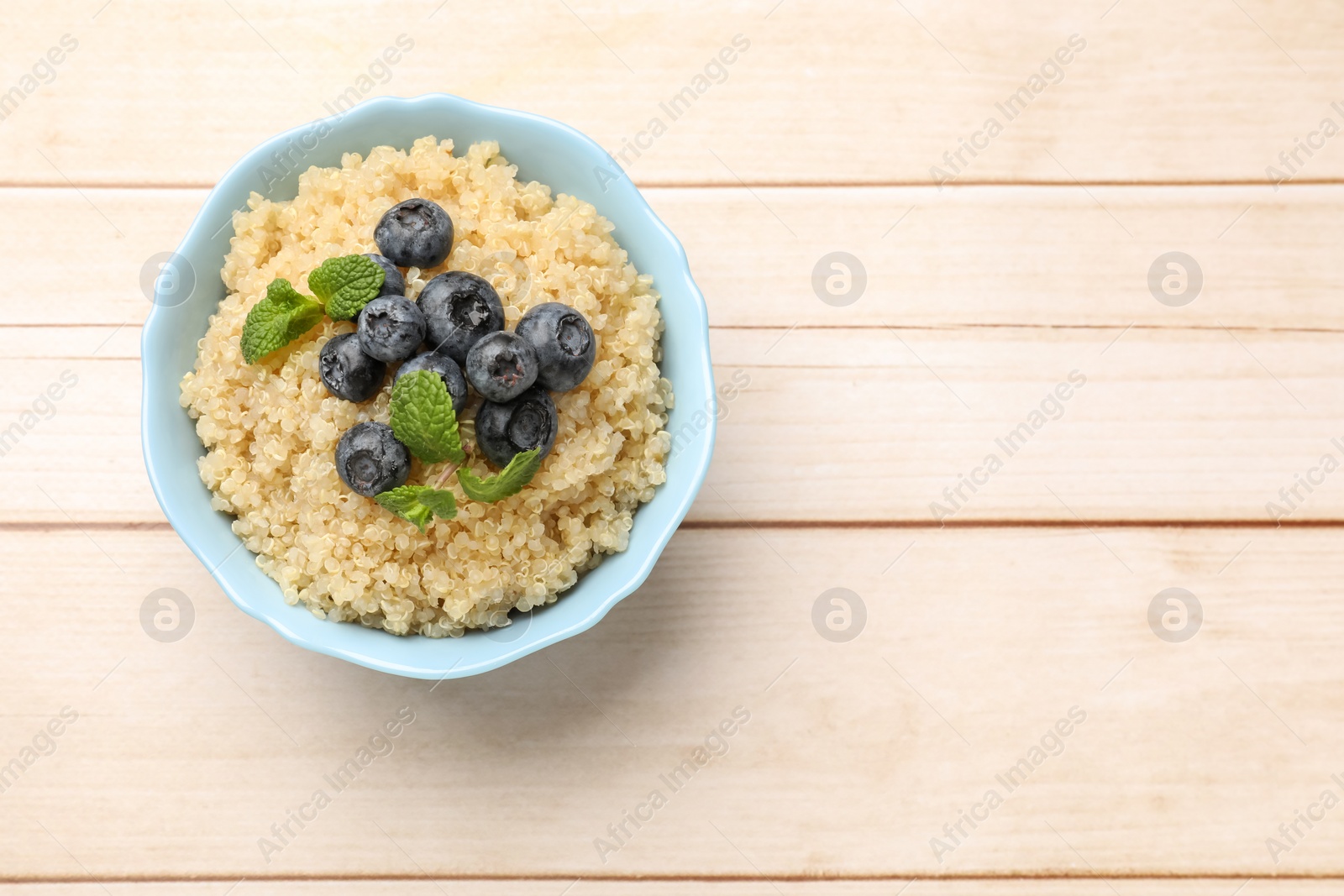 Photo of Tasty quinoa porridge with blueberries and mint in bowl on light wooden table, top view. Space for text