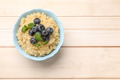 Photo of Tasty quinoa porridge with blueberries and mint in bowl on light wooden table, top view. Space for text