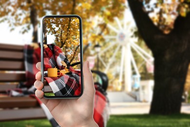 Image of Woman taking picture of wooden bench with cup and plaid in park on autumn day, closeup