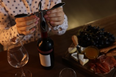 Photo of Romantic dinner. Woman opening wine bottle with corkscrew at table indoors, closeup