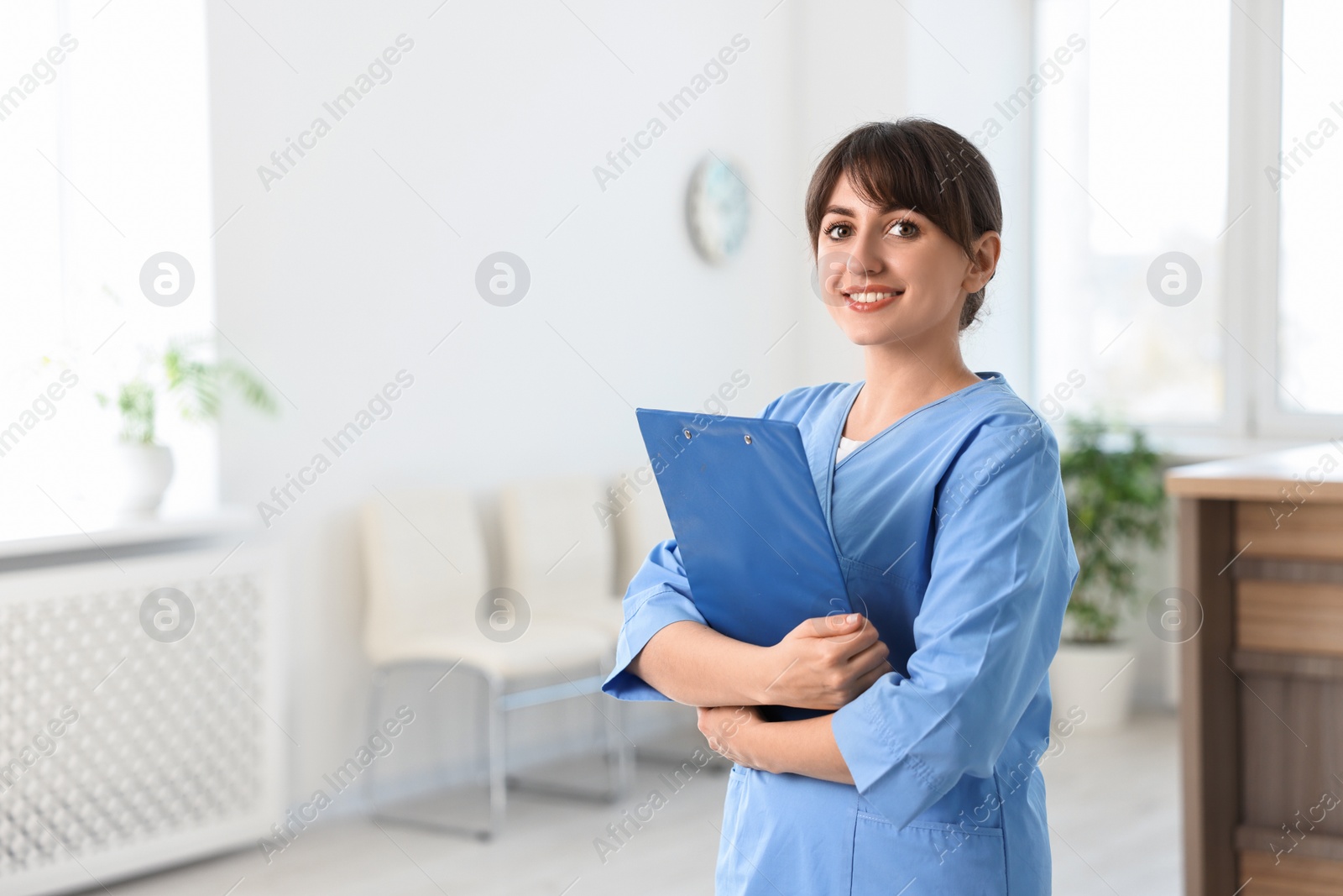 Photo of Portrait of smiling medical assistant with clipboard in hospital. Space for text