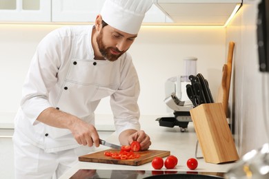 Photo of Professional chef cutting tomatoes in stylish kitchen