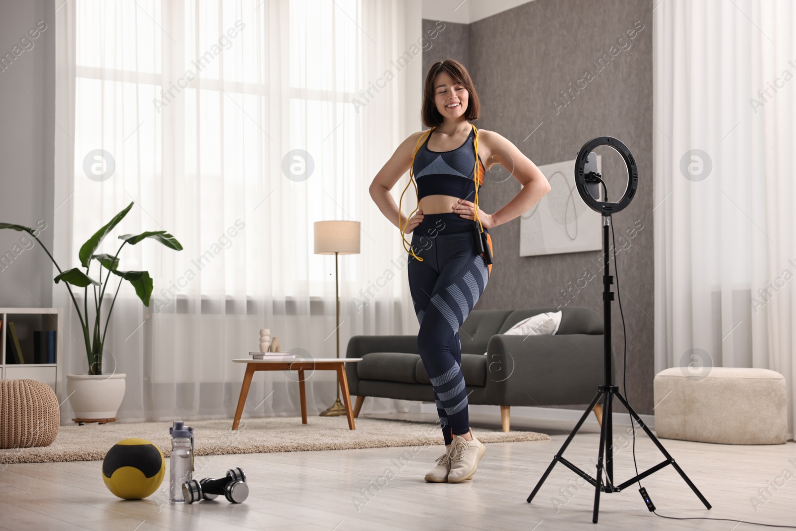 Photo of Happy sports blogger with skipping rope streaming online fitness lesson with smartphone at home