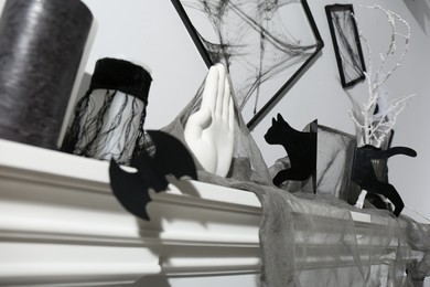Photo of Black frames with cobweb on white wall and different Halloween decor on fireplace indoors, closeup