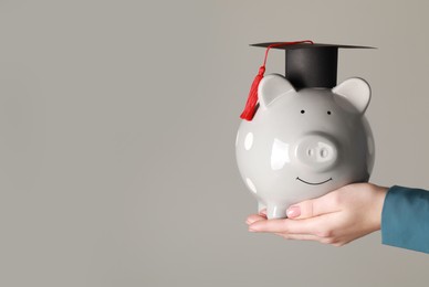 Photo of Man holding piggy bank and graduation cap against grey background, closeup with space for text. Scholarship concept