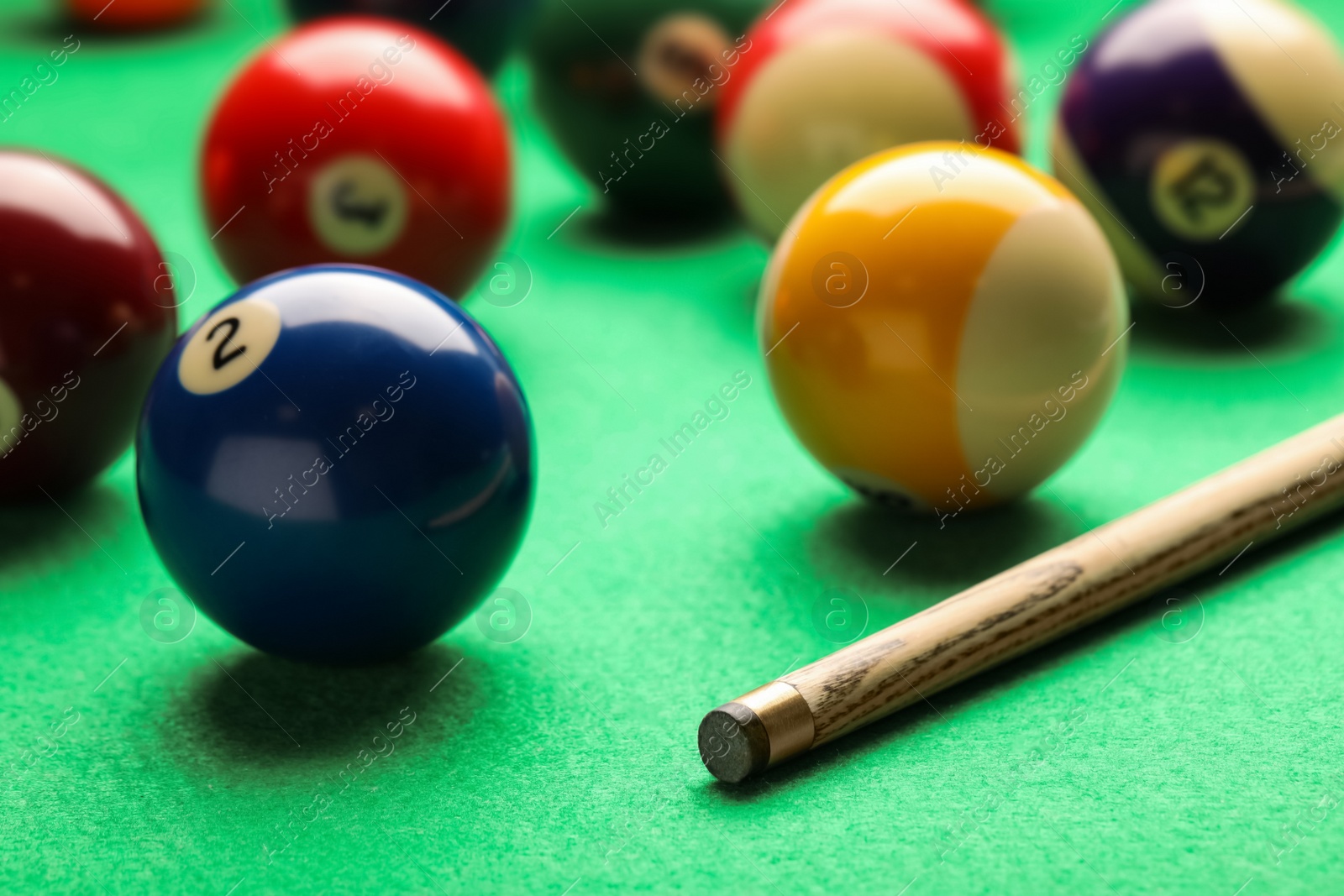 Photo of Many colorful billiard balls and cue on green table, closeup