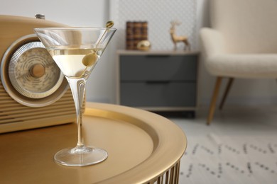 Photo of Martini cocktail with olive and retro radio receiver on table in room, space for text. Relax at home