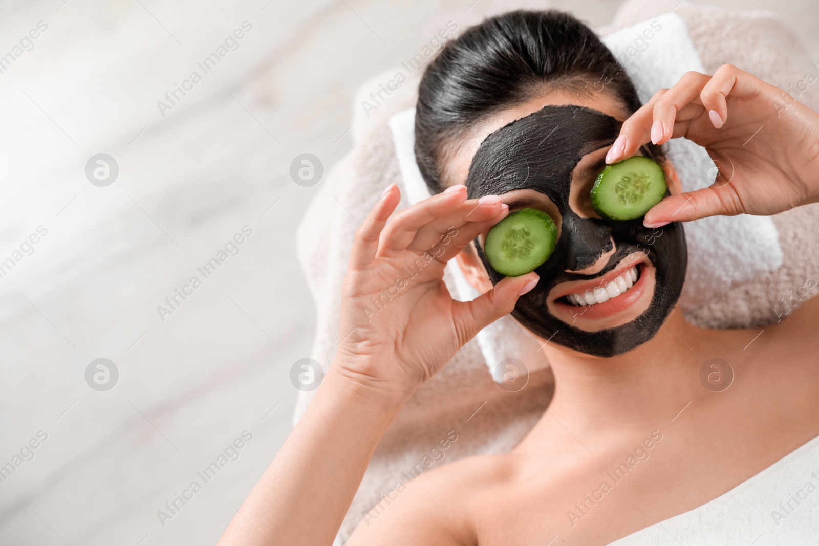 Photo of Beautiful woman with black mask on face and cucumber slices relaxing in spa salon, top view. Space for text