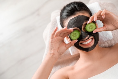 Beautiful woman with black mask on face and cucumber slices relaxing in spa salon, top view. Space for text