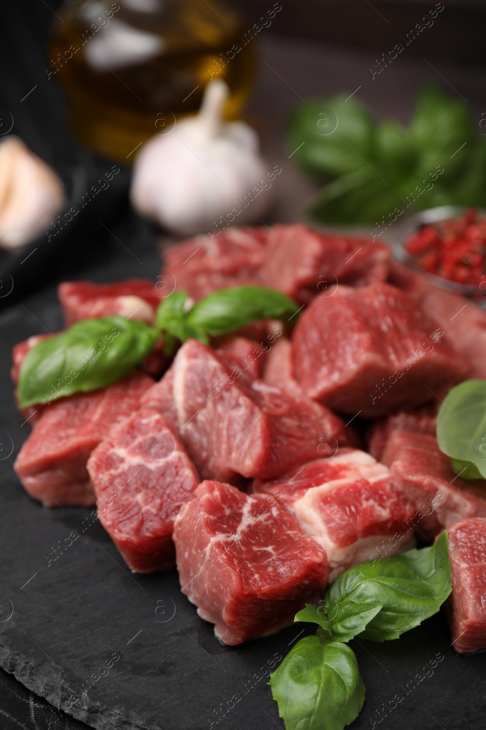Photo of Cut fresh beef meat and basil leaves on slate plate, closeup
