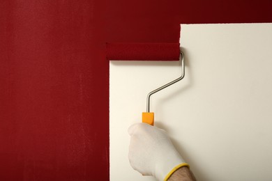 Photo of Man applying red paint with roller brush on white wall, closeup