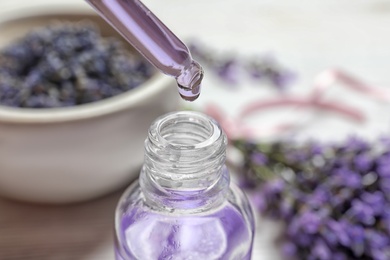 Natural oil dripping into bottle and lavender flowers on table, closeup. Cosmetic product