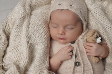 Photo of Adorable newborn baby with toy bear sleeping on knitted plaid, top view