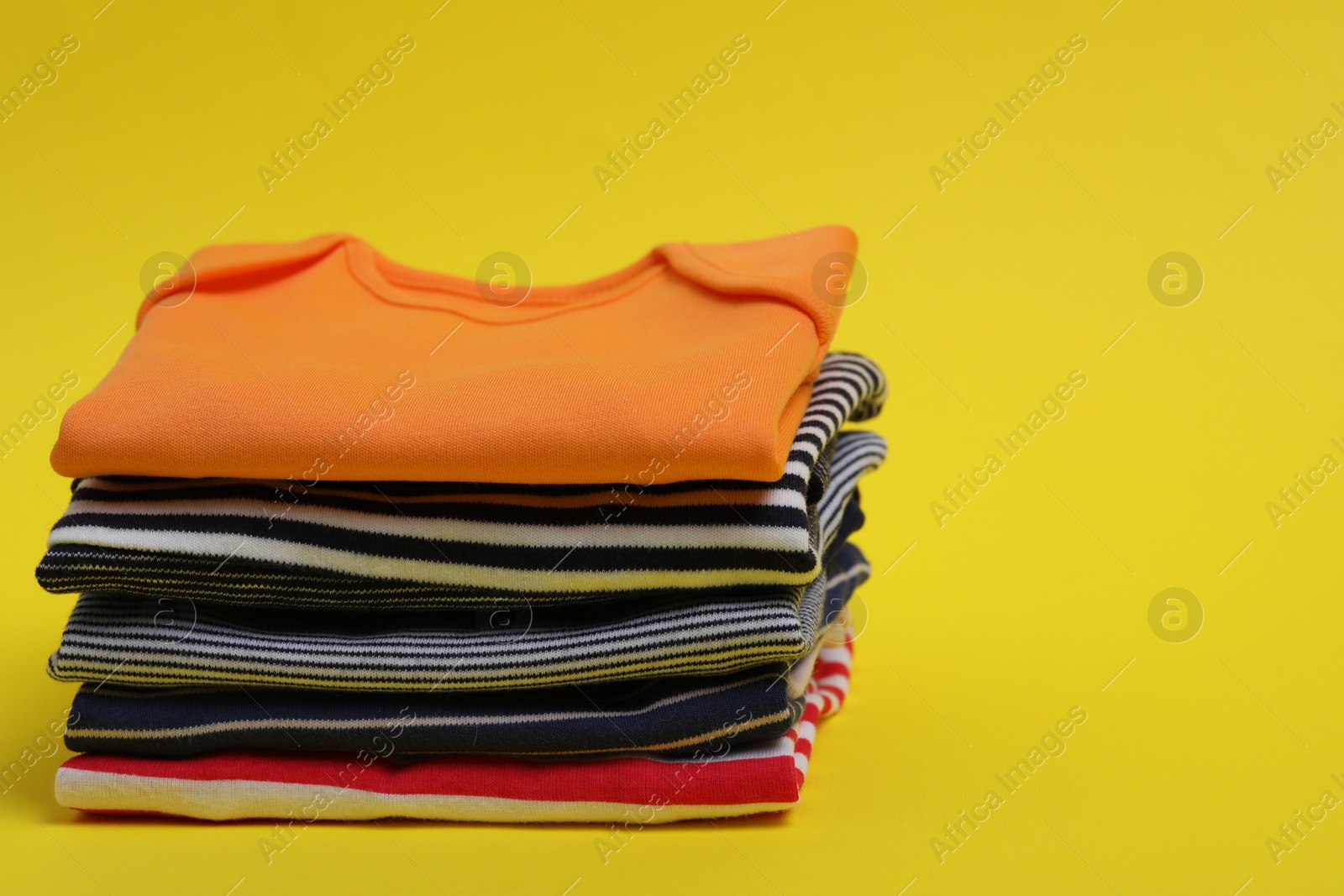 Photo of Stack of clean baby clothes on yellow background. Space for text