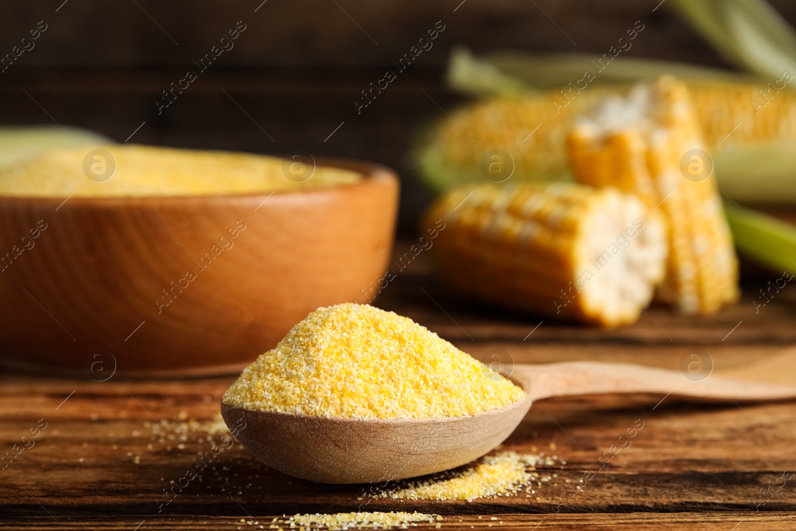 Photo of Cornmeal in spoon on wooden table, closeup