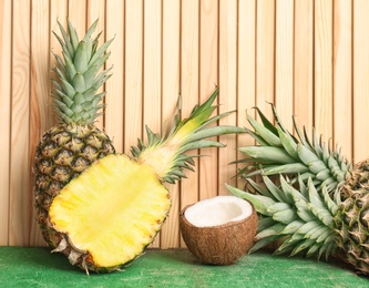 Fresh pineapples and coconut on table against wooden wall