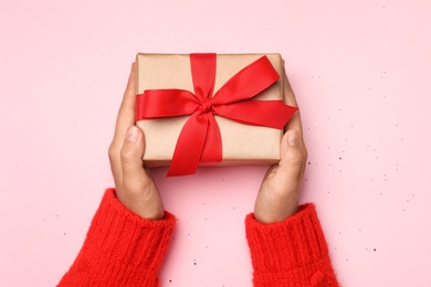 Photo of Young woman holding Christmas gift on pink background, top view