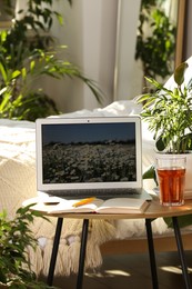 Photo of Laptop, glass of drink, notebook and pen on wooden side table in bedroom