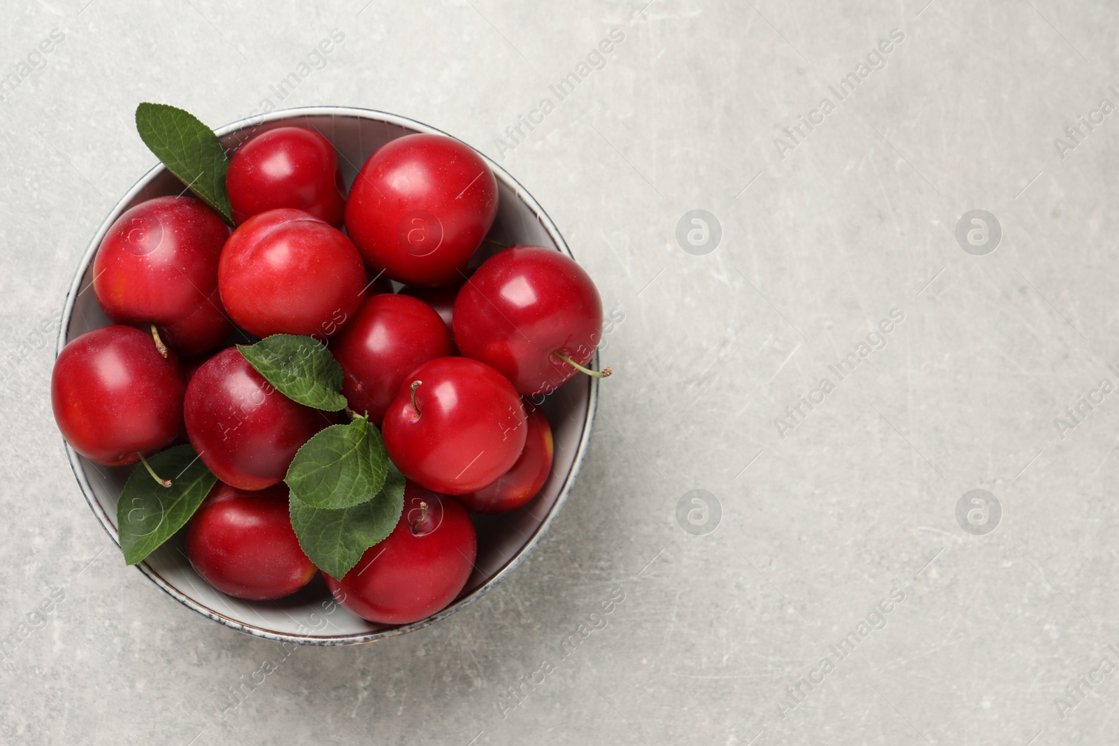 Photo of Delicious ripe cherry plums with leaves on light table, top view. Space for text