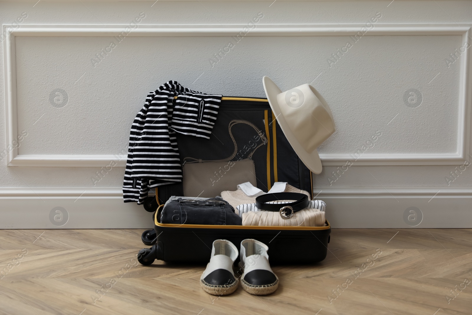 Photo of Open suitcase with folded clothes, accessories and shoes near white wall indoors
