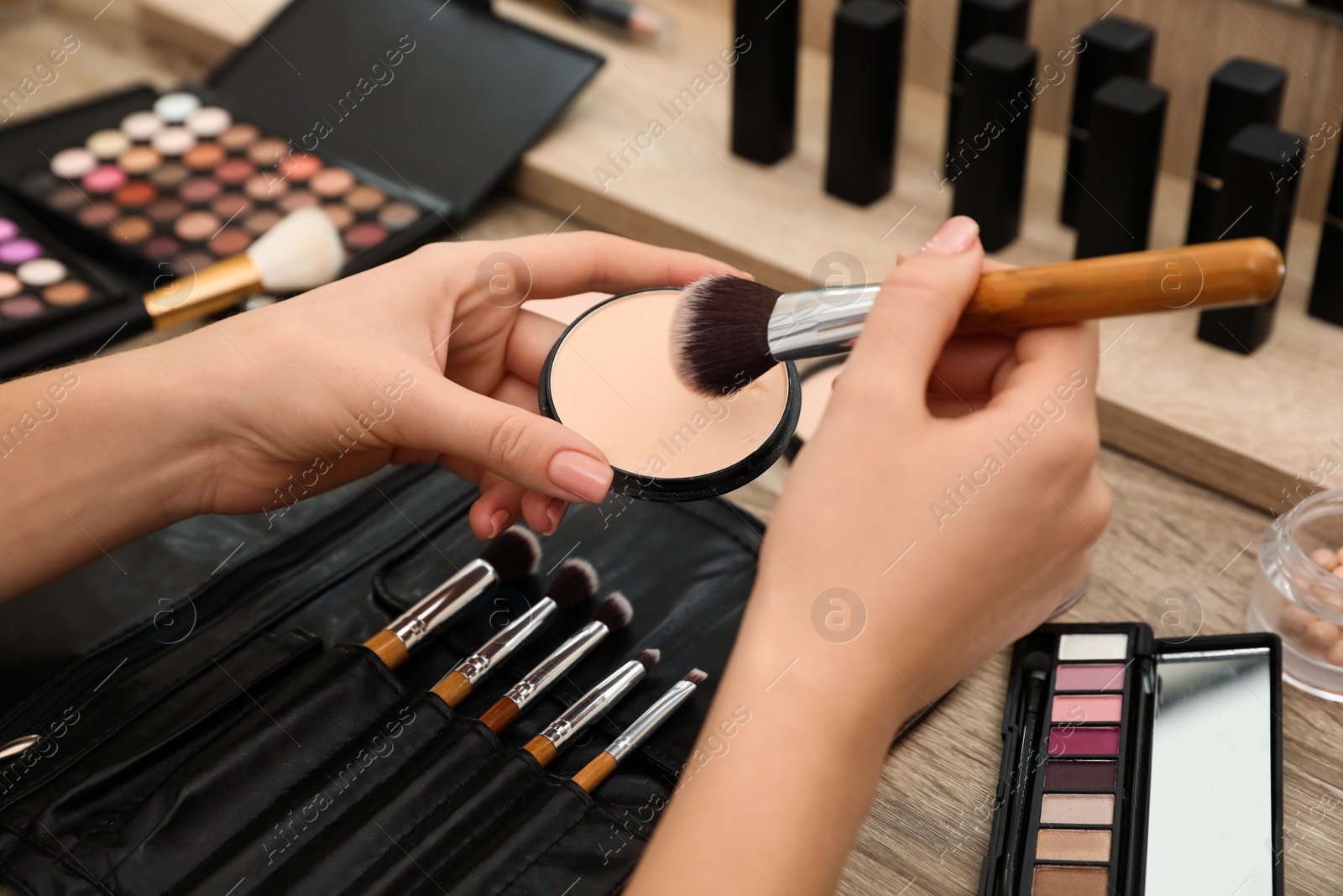 Photo of Professional makeup artist with powder and brush at wooden table, closeup