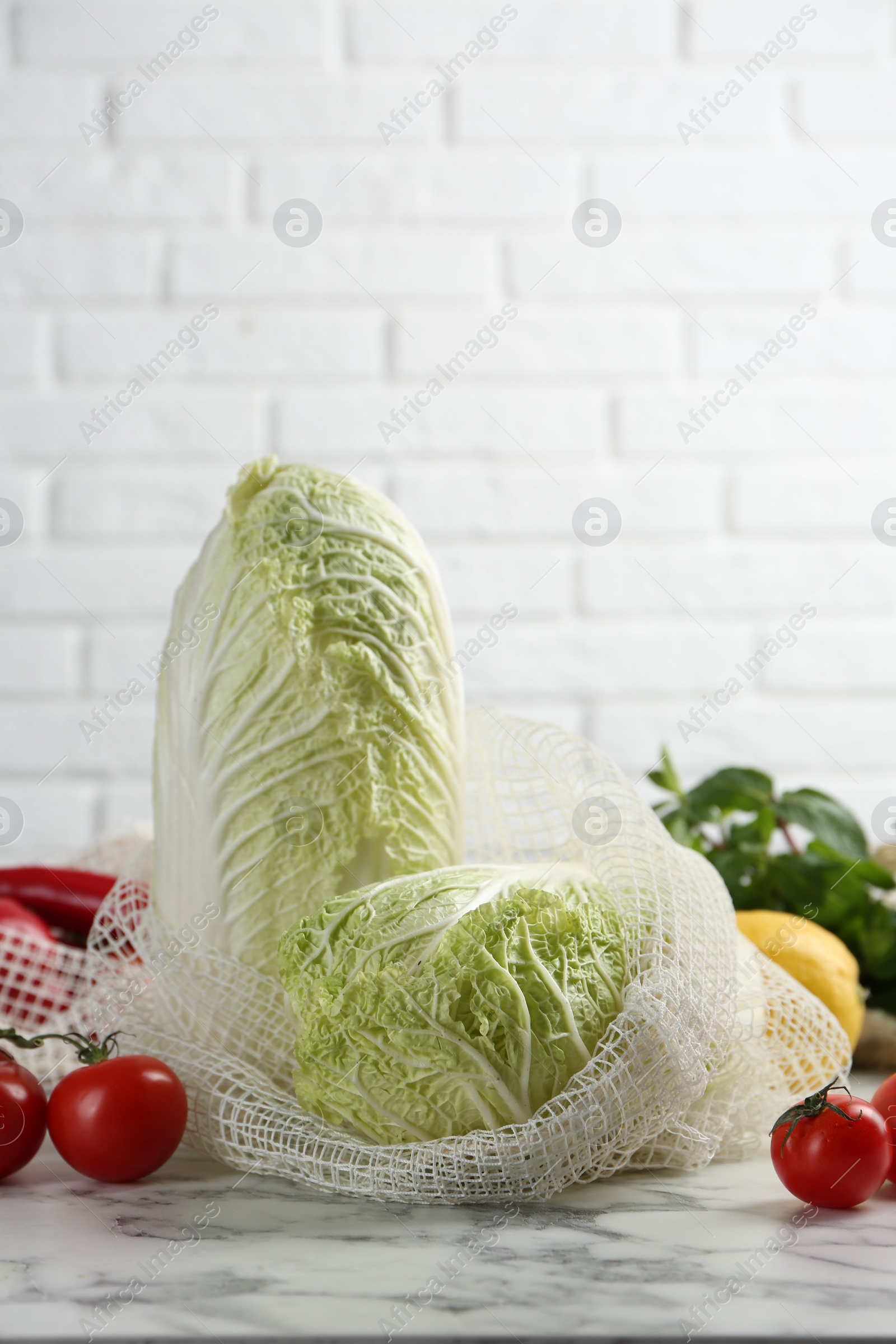 Photo of Fresh Chinese cabbages and other vegetables on white marble table near brick wall