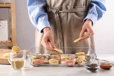 Photo of Woman cooking chicken breasts with lemon at grey marble table, closeup