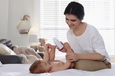 Mother with bottle of dusting powder and her cute baby at home, space for text