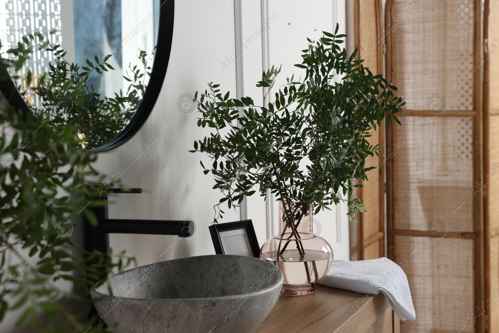 Photo of Eucalyptus branches and towel near stylish vessel sink on bathroom vanity. Interior design