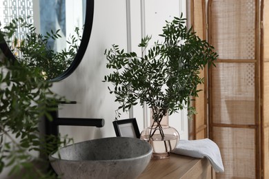 Eucalyptus branches and towel near stylish vessel sink on bathroom vanity. Interior design