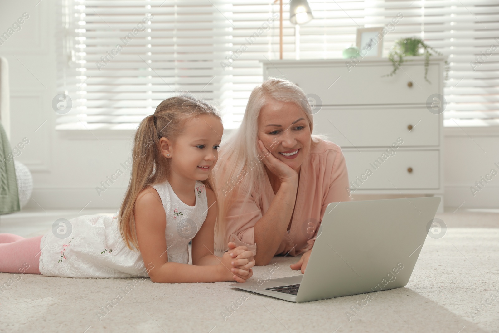 Photo of Happy grandmother and her granddaughter using  laptop together on floor at home