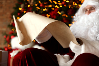 Photo of Santa Claus reading wish list against blurred festive lights, closeup