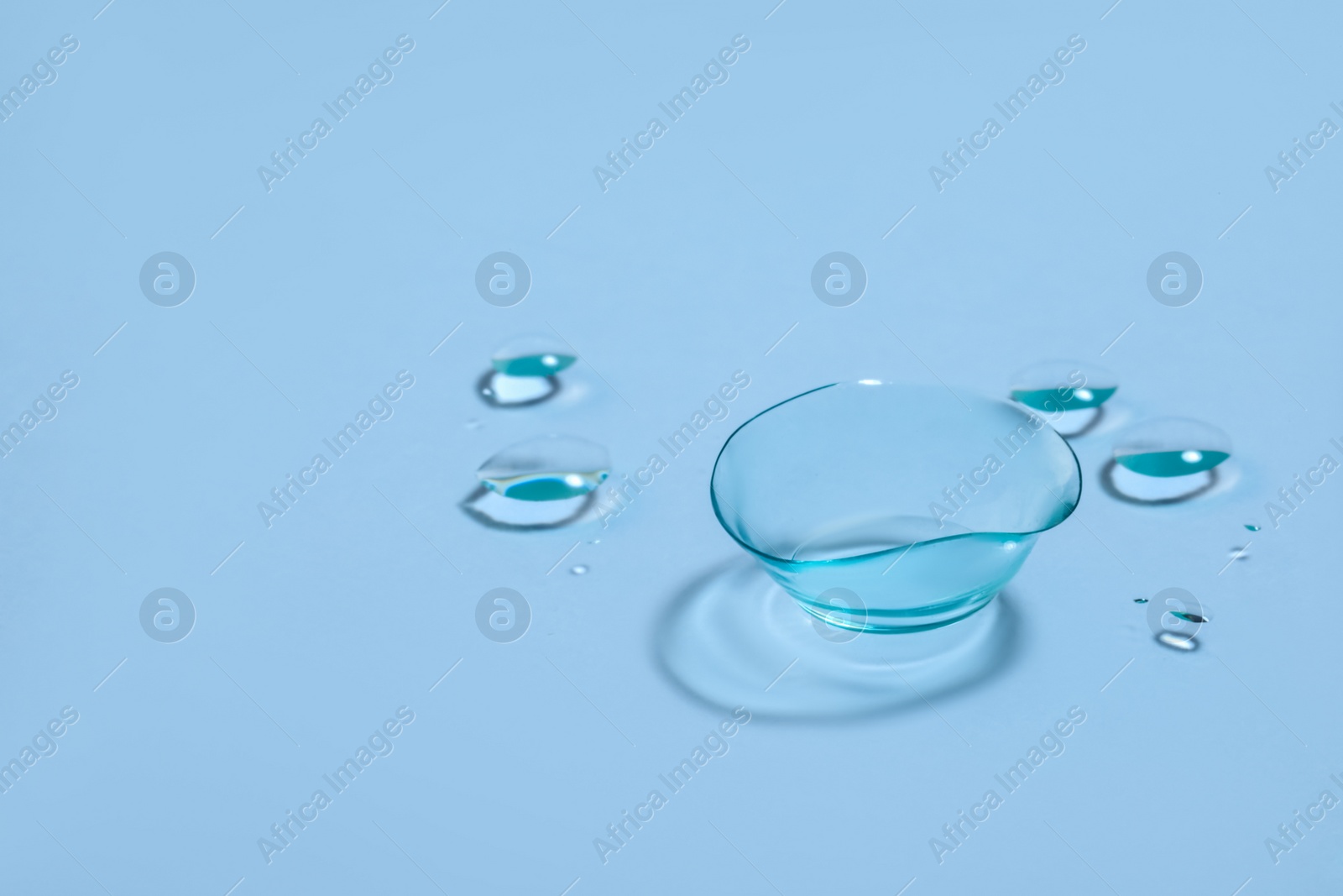 Photo of One contact lens and drops of water on light blue background. Space for text