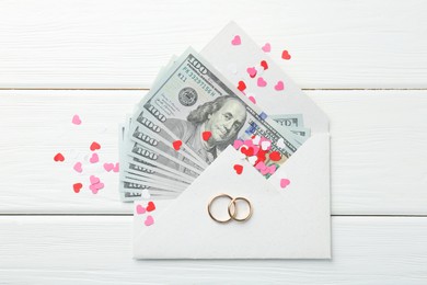 Photo of Honeymoon concept. Two golden rings, money and cutout hearts on white wooden table, flat lay