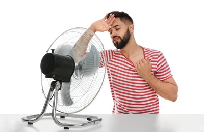 Photo of Man suffering from heat in front of fan on white background. Summer season