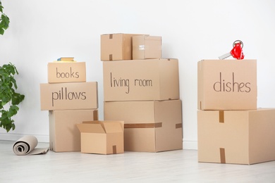 Photo of Cardboard boxes and household stuff near white wall indoors. Moving day