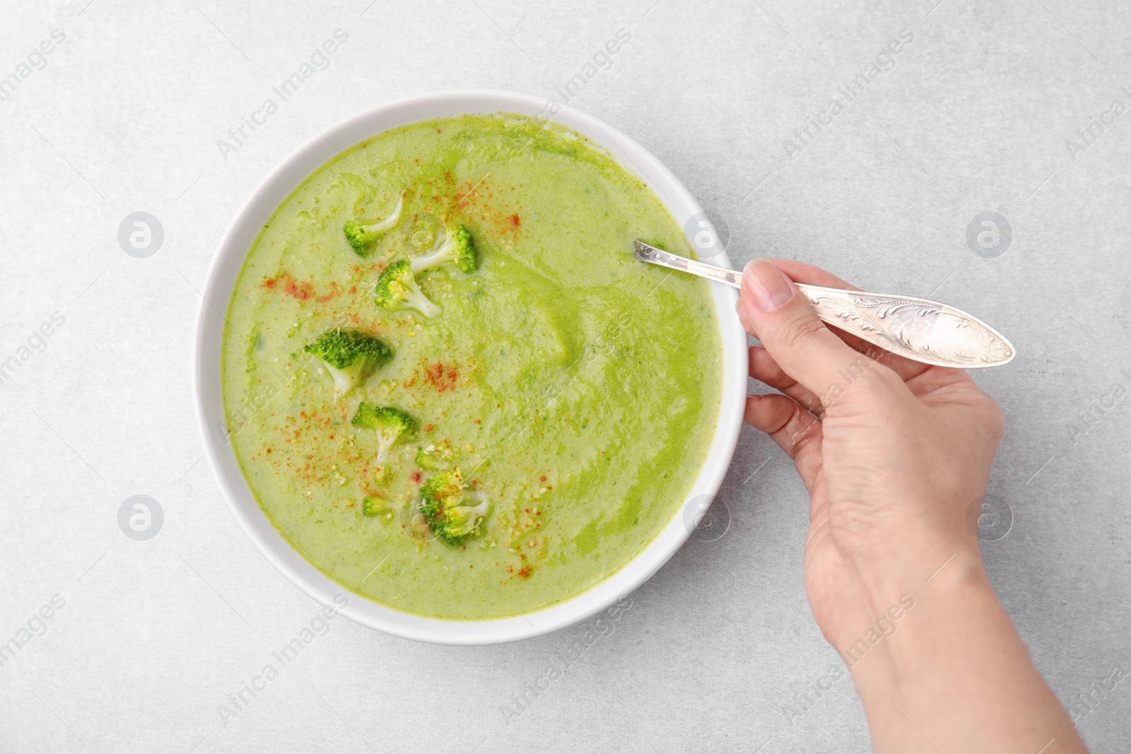 Photo of Woman with bowl of delicious broccoli cream soup at table, top view